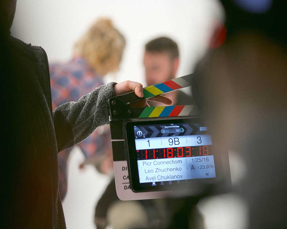 A director's clapperboard in front of two actors on a set.