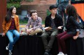 Four children sit on a black stage in conversation.