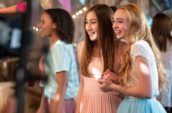 Three young smiling girls wearing dresses standing at a party.