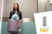 A woman with long dark hair stands in an elevator holding a blue basket with children's toys.